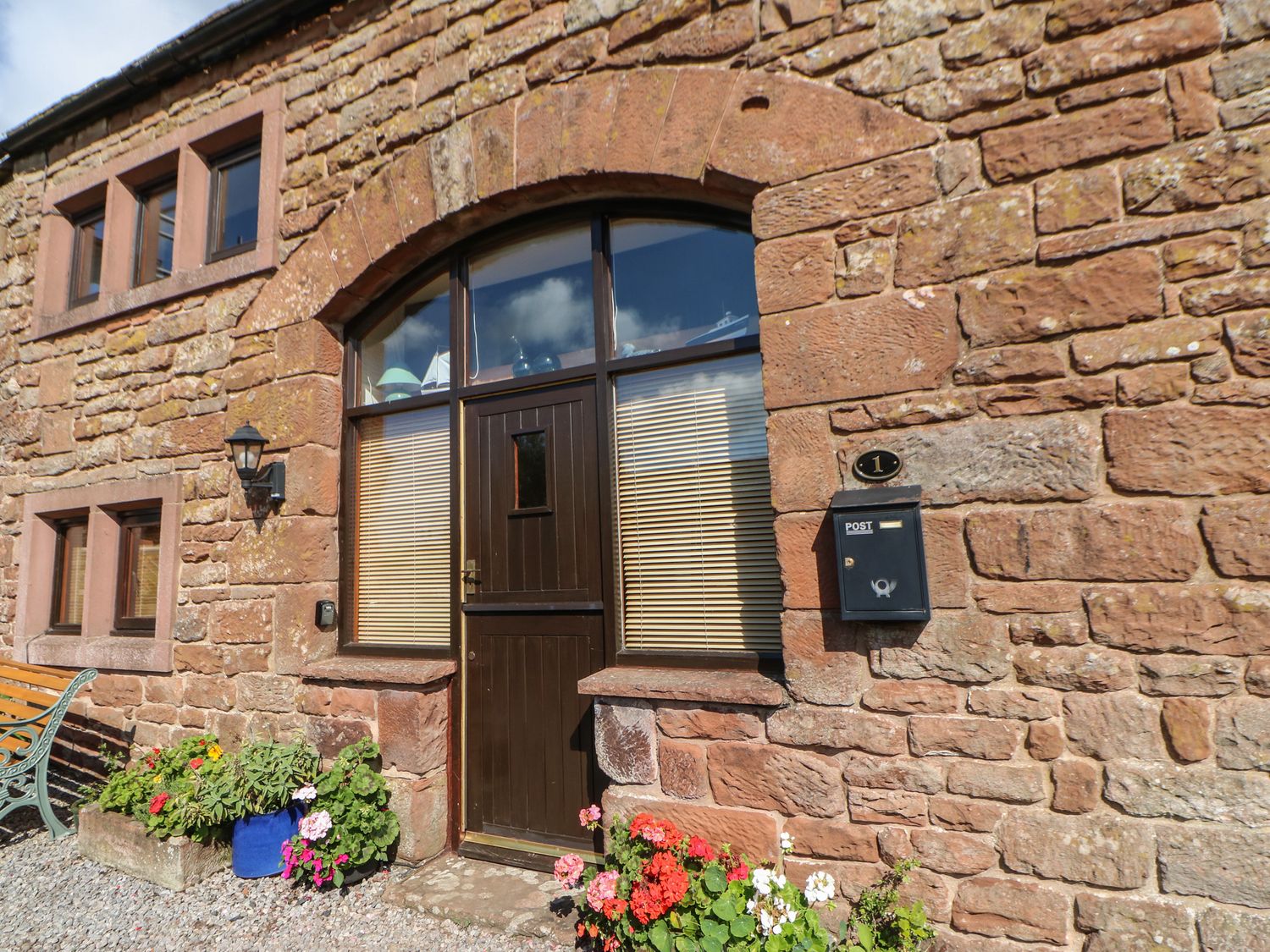 The exterior of a stone building with a dark wooden door flanked by windows and flower pots near the entrance at 1 Yew Tree Cottages in Langwathby