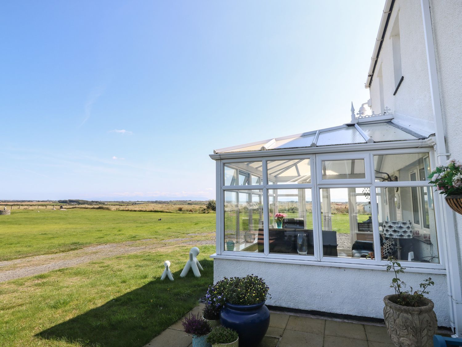 A glass conservatory attached to a white house with potted plants outside and a grassy field in the background at Trewan House Bryngwran near Rhosneigr Rhosneigr