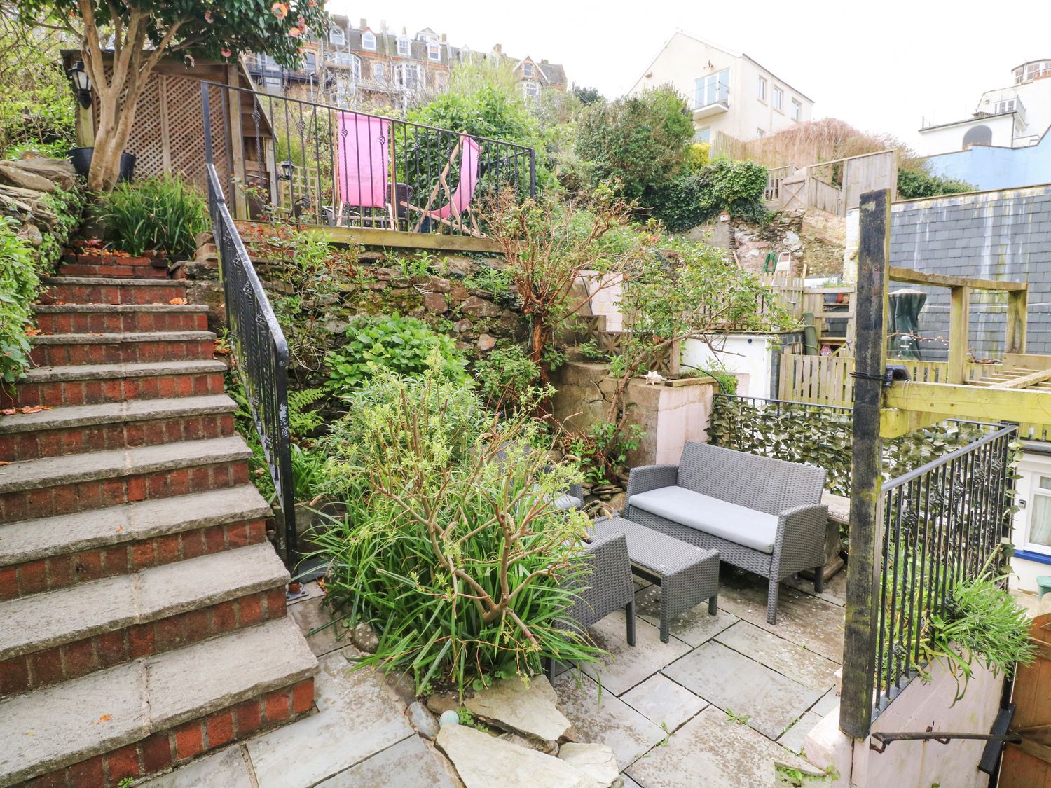 An outdoor patio area with grey wicker furniture and two pink chairs on a raised deck at Harbour Cottage in Ilfracombe