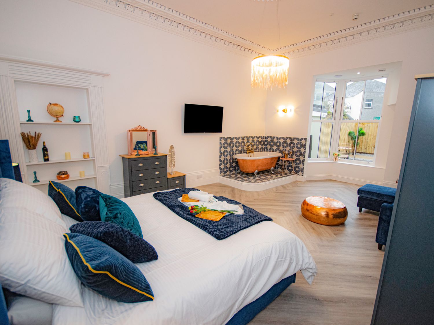 A bedroom with a bed pillows and a bathtub with patterned tiles a dresser and a television at Mews Retreat in Camborne