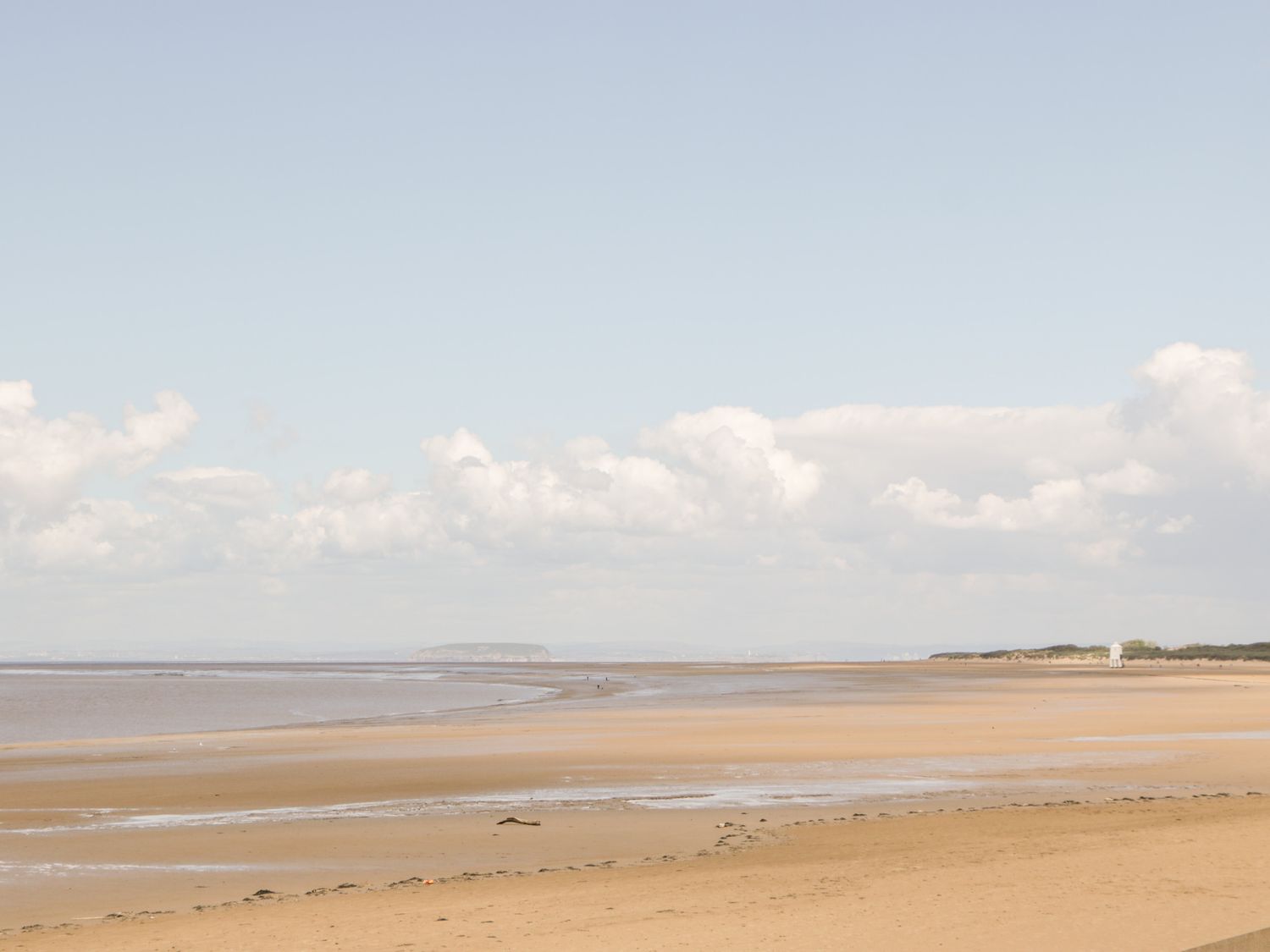 A sandy beach with shallow water and a small white building in the distance at Seacider in Burnham-On-Sea
