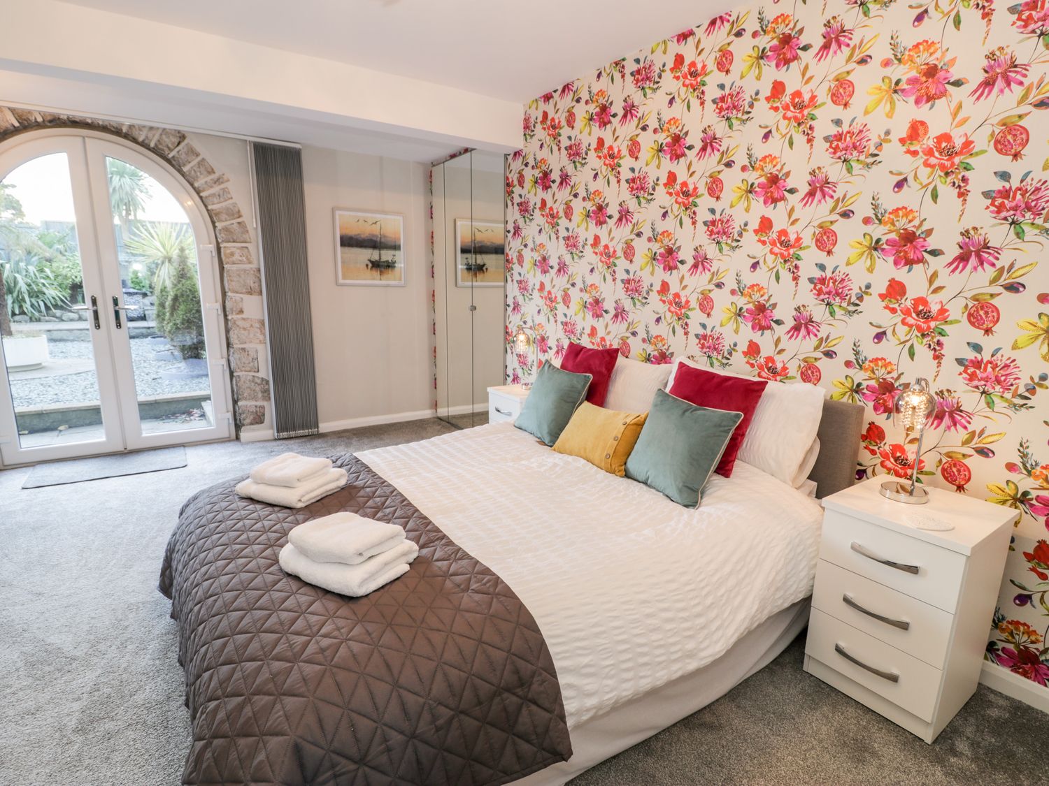 A bedroom with a bed with pillows and folded towels next to white nightstands and a glass door at The Chalet in Benllech