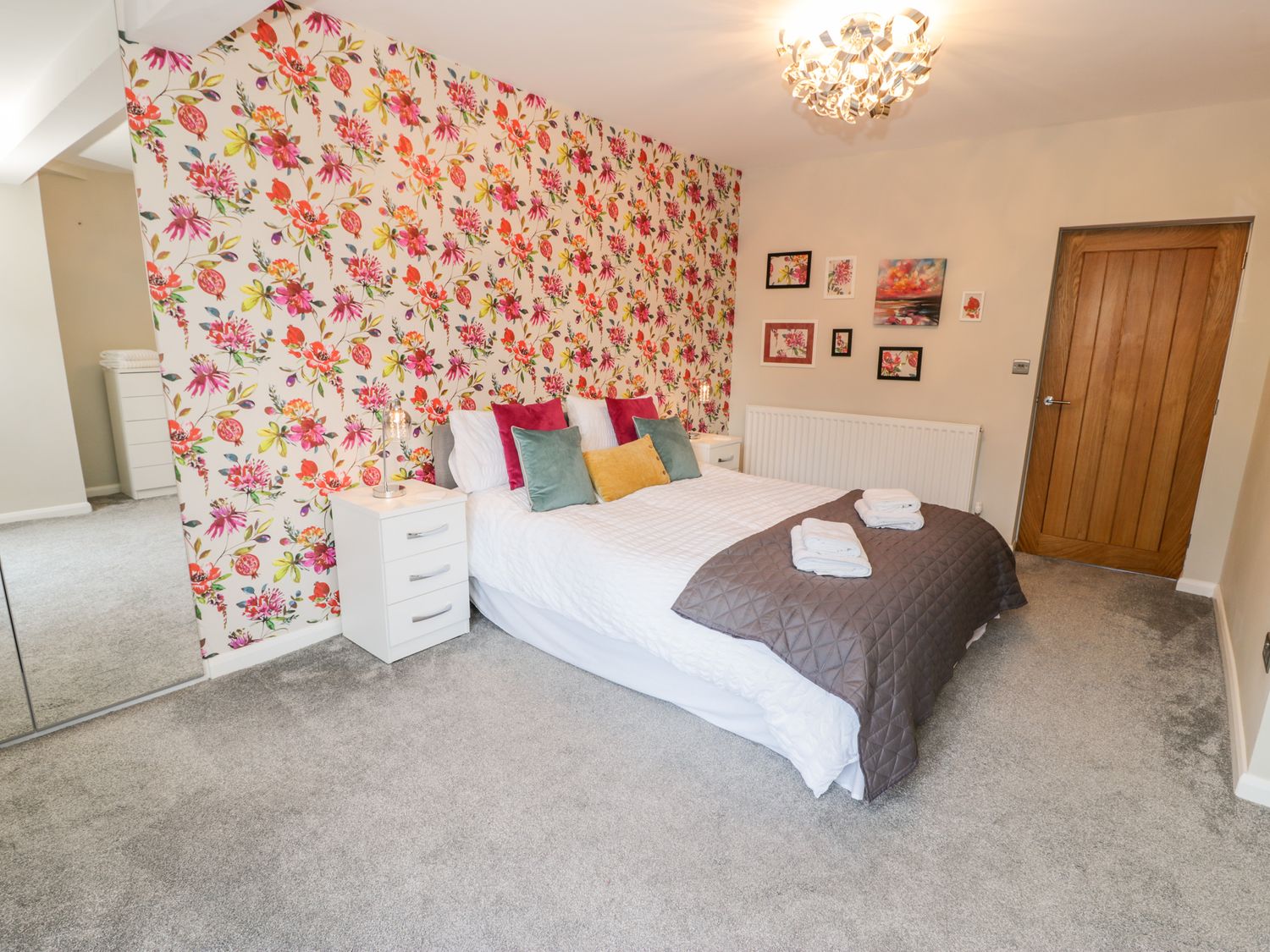 A bedroom with a double bed with pillows and a blanket floral wallpaper and framed pictures on the wall at The Chalet in Benllech