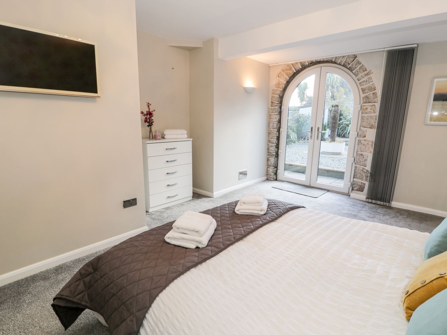 A bedroom with a bed and folded towels a chest of drawers and arched glass doors at The Chalet in Benllech