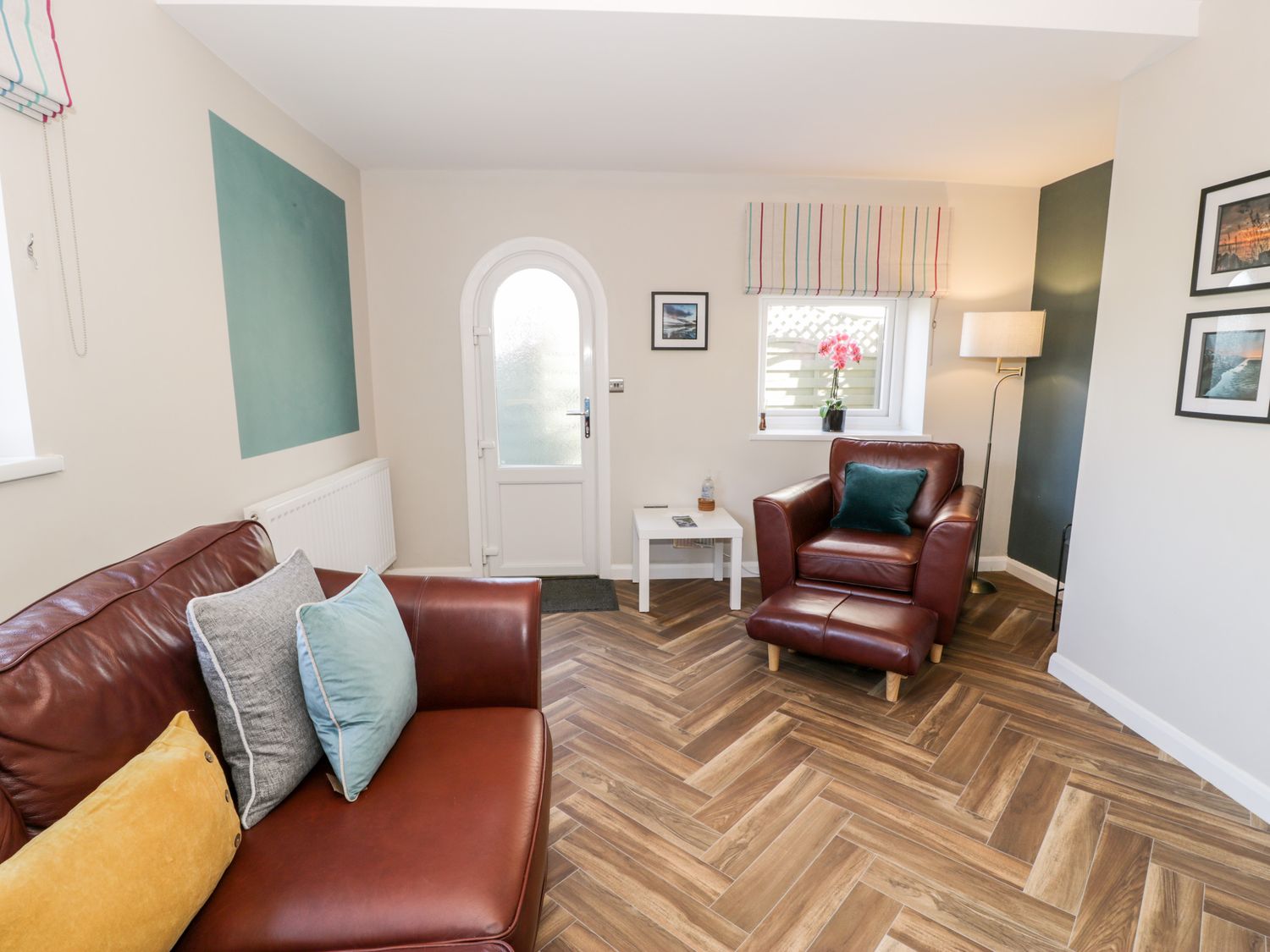 A sitting room with leather sofas pillows a side table with a water bottle and lamp at The Chalet in Benllech
