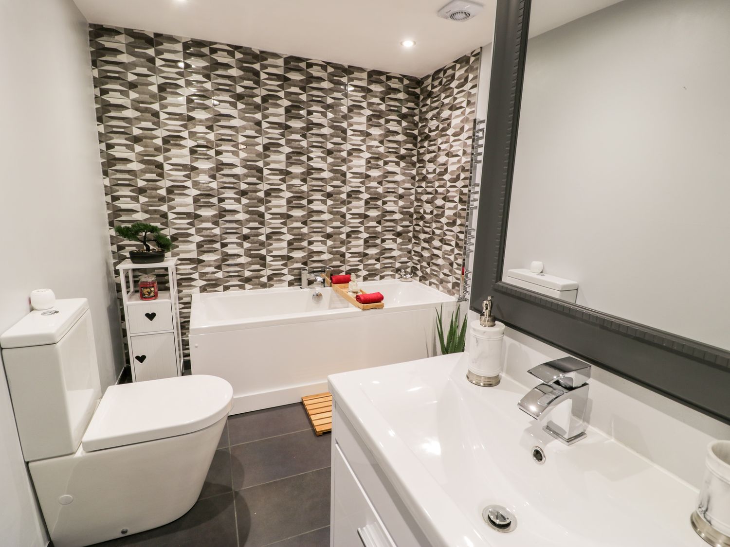 A bathroom with a white bathtub tiled wall and a white toilet at The Chalet in Benllech