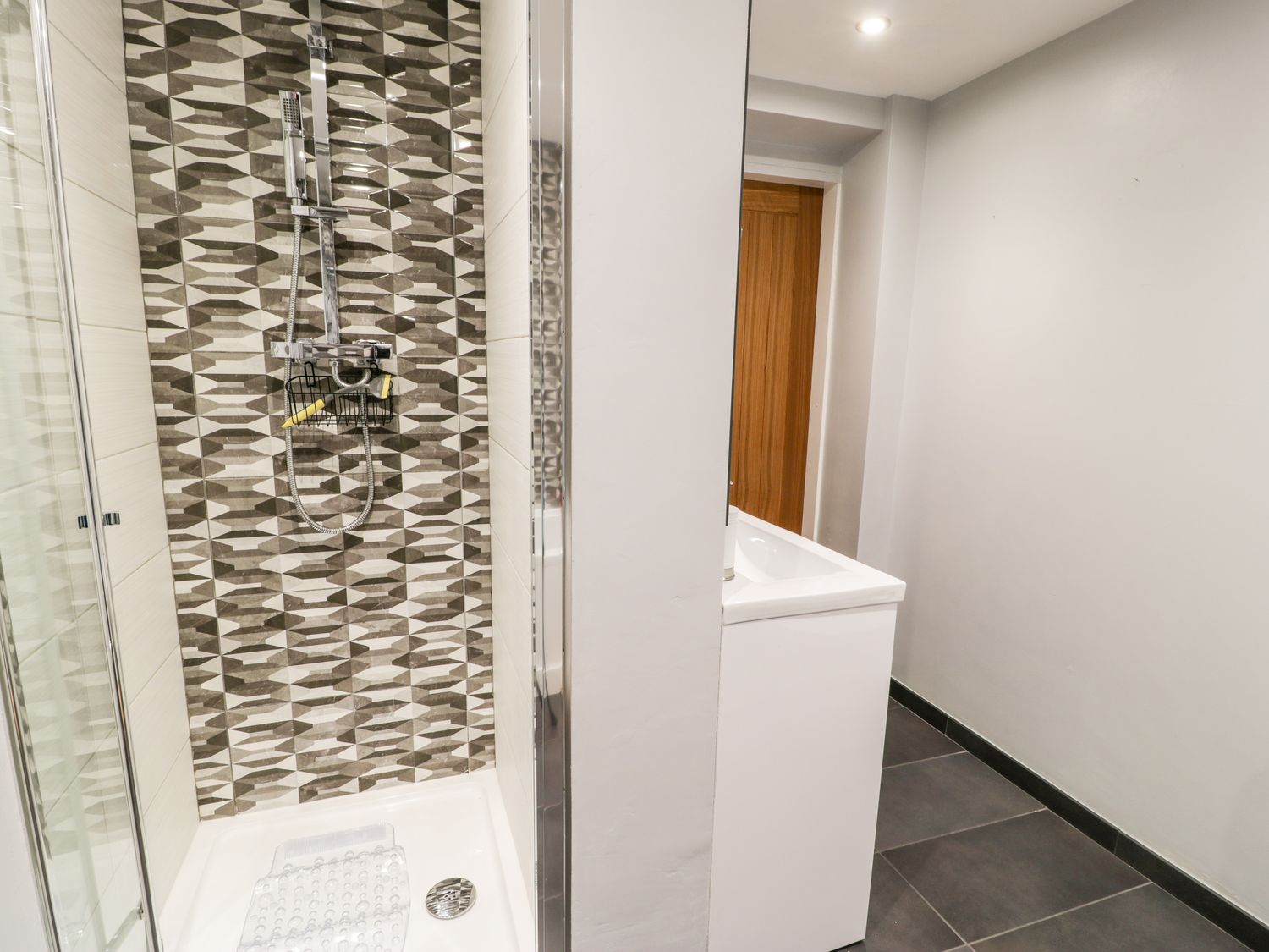 A bathroom with a shower area with patterned tiles and a sink next to a wooden door at The Chalet in Benllech