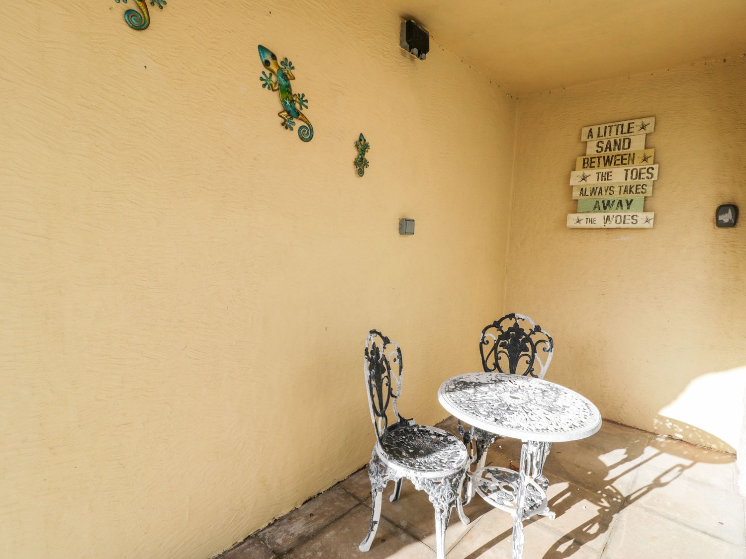 A small outdoor seating area with two metal chairs and a round table on a tiled floor with wall decorations at The Chalet in Benllech
