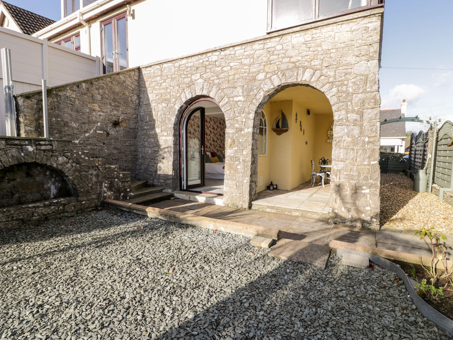 A stone patio with arches leading to a room and a small seating area at The Chalet in Benllech