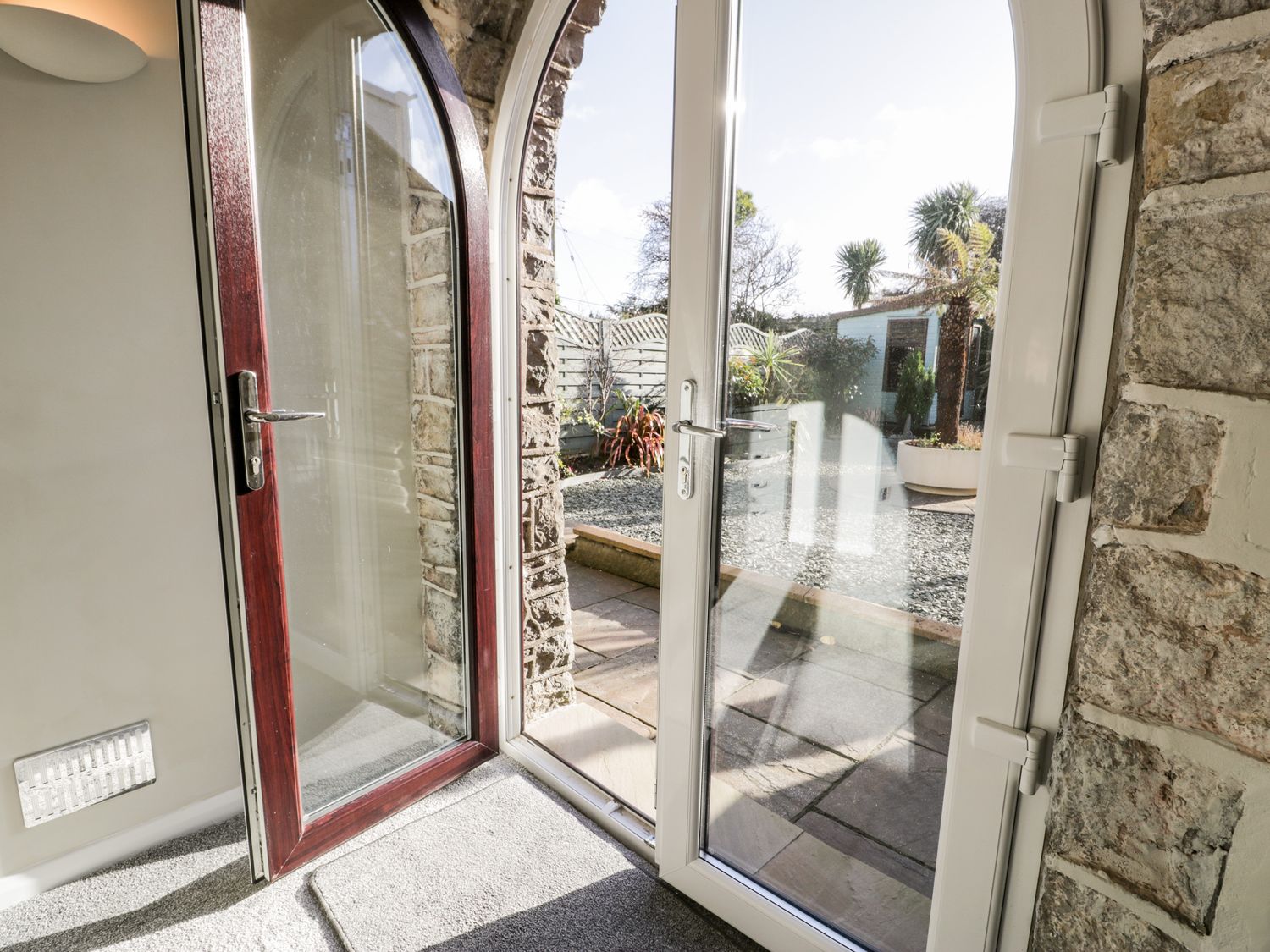 An open glass door leading to a garden with plants and a shed at The Chalet in Benllech