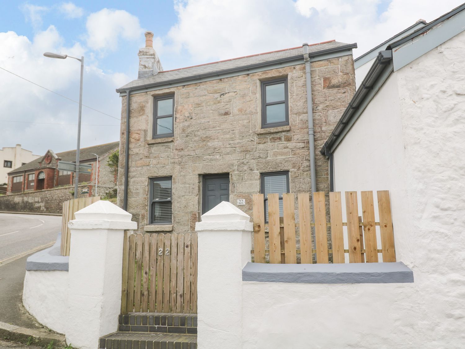 A stone house with wooden gate and white wall on a street corner at Rose Bank Cottage in St Just