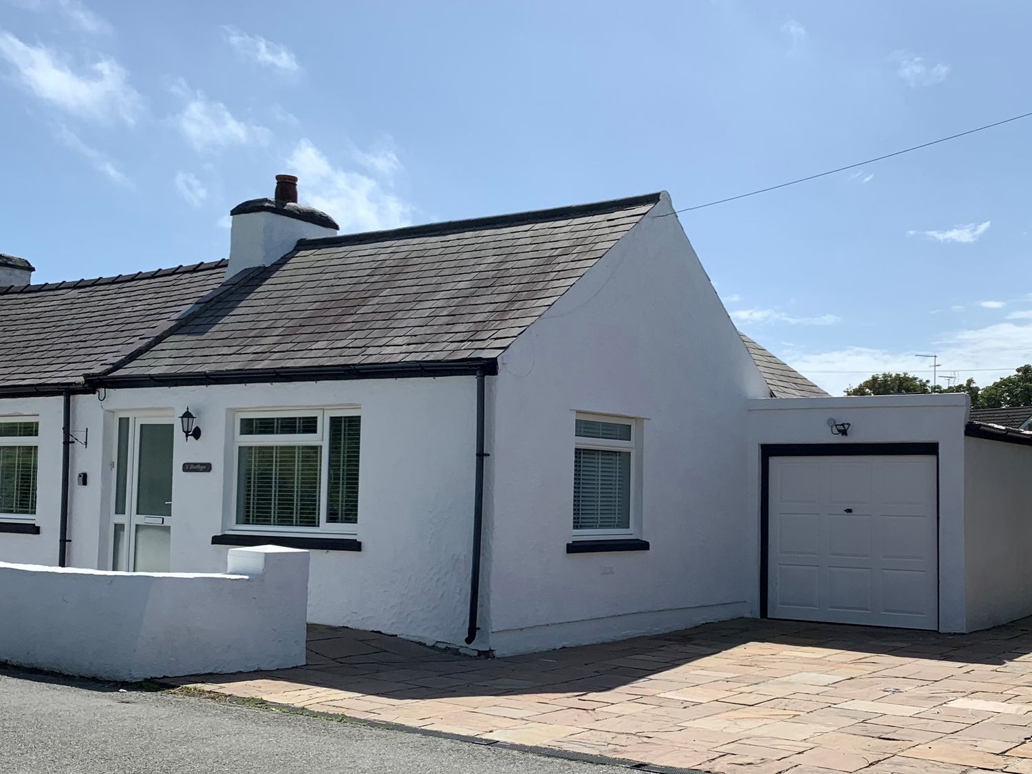 A white house with a slate roof and attached garage on a paved driveway at 3 Tai Newydd in Llanfaelog near Rhosneigr