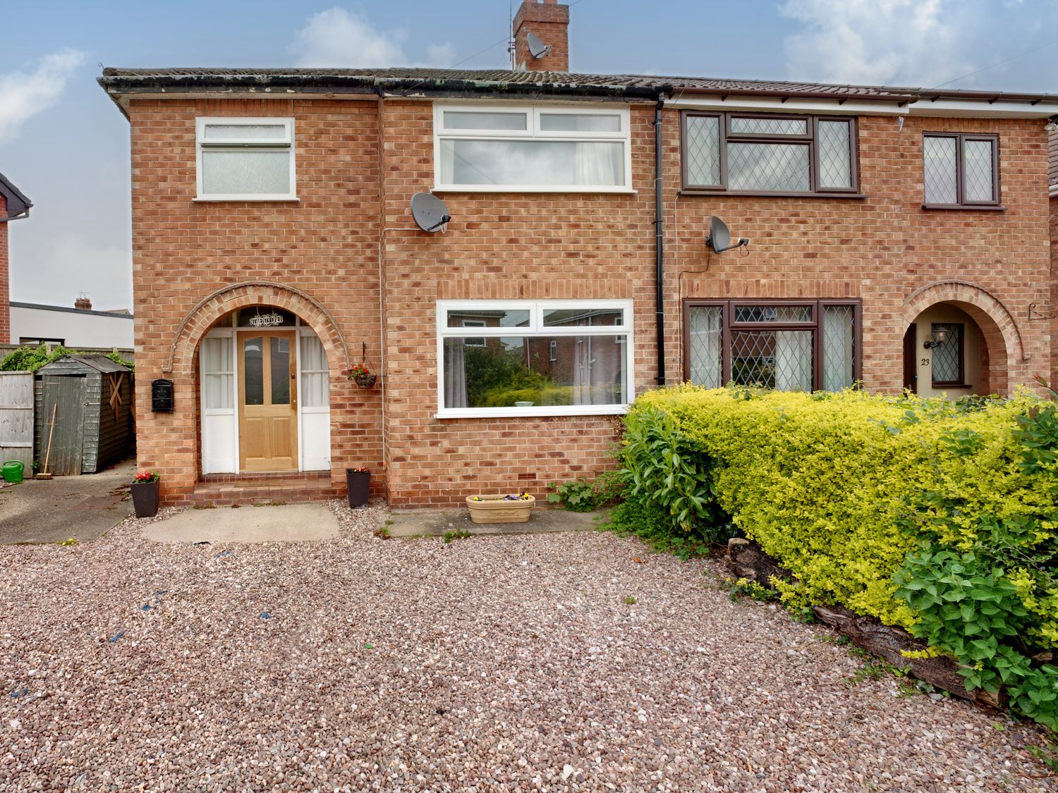 A brick terraced house with pebble driveway and green bushes at The Hawthorns in Christleton