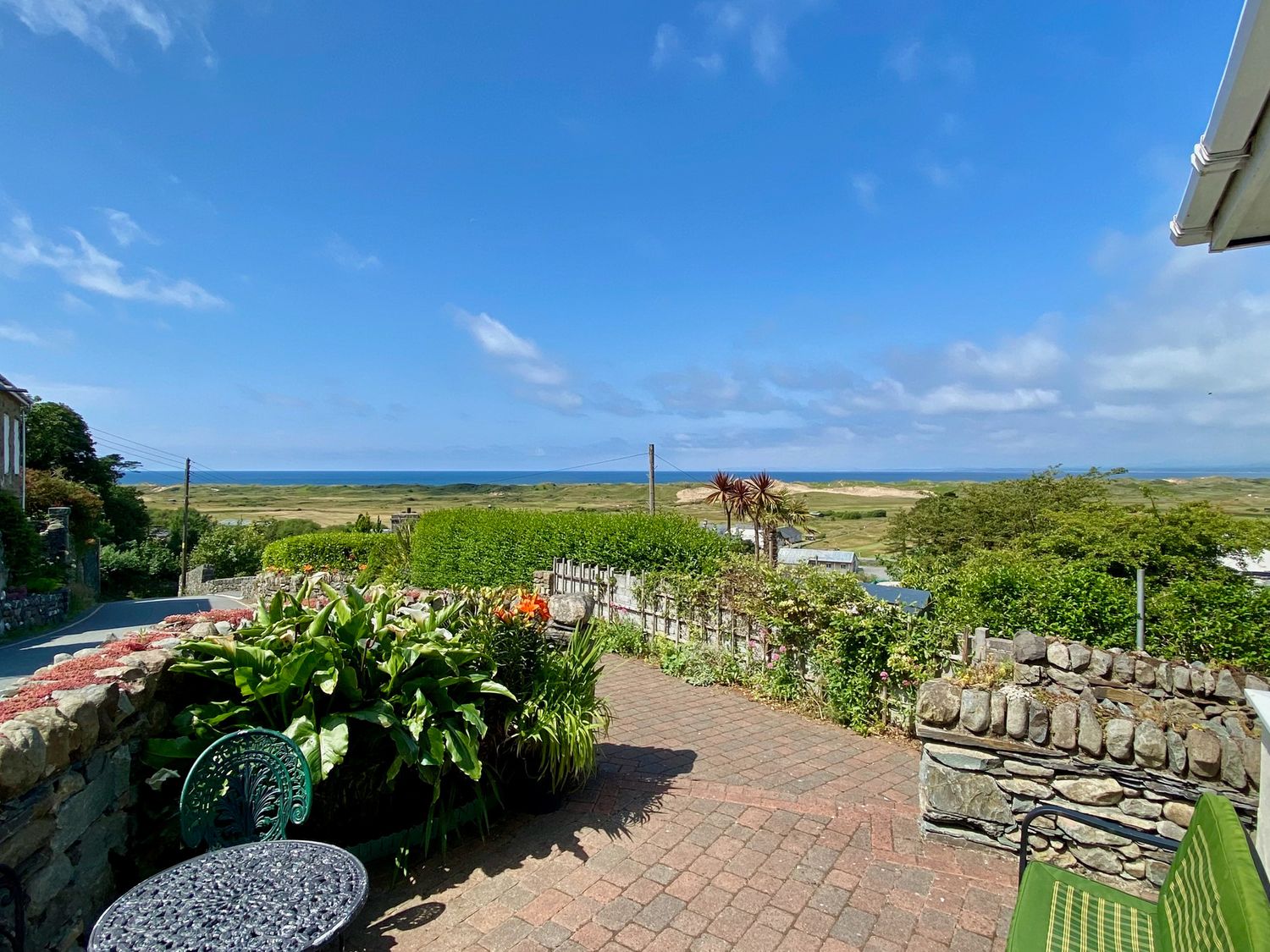 An outdoor patio with metal table and chair surrounded by stone walls and plants with a view of fields and sea at Stoneycroft in Harlech