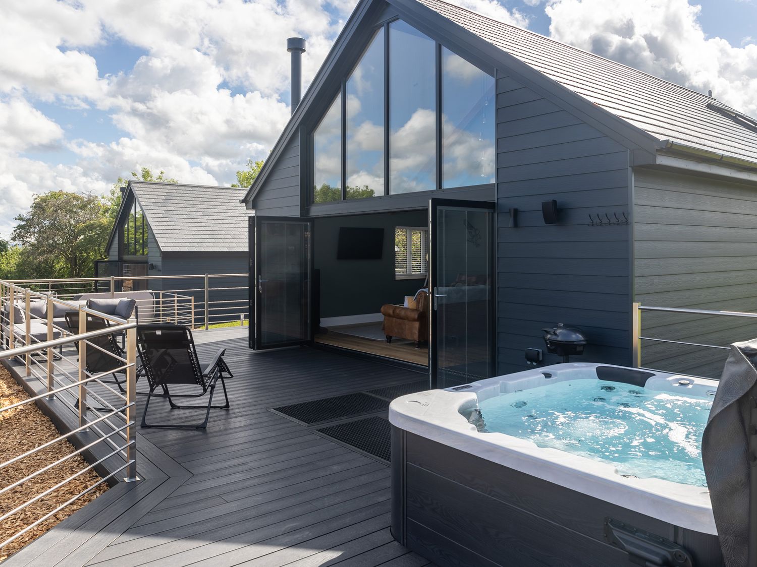 An outdoor deck with a hot tub lounge chairs and an open door to a living room at Eagles Peak in Allerton near Thornton-Le-Dale