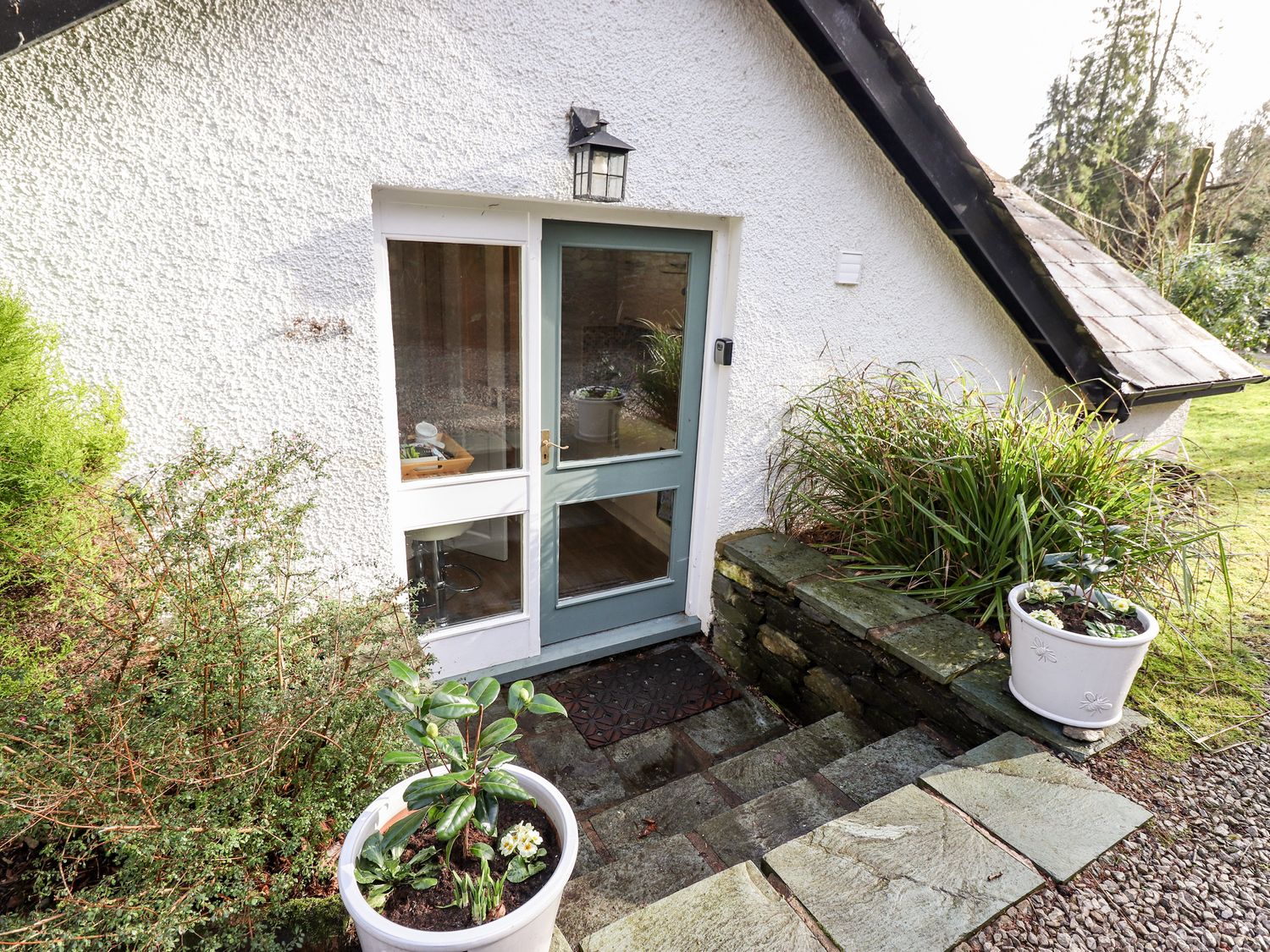 A stone stairway leading to a glass door with plants in white pots on either side at Peony Cottage in Lakeside near Newby Bridge