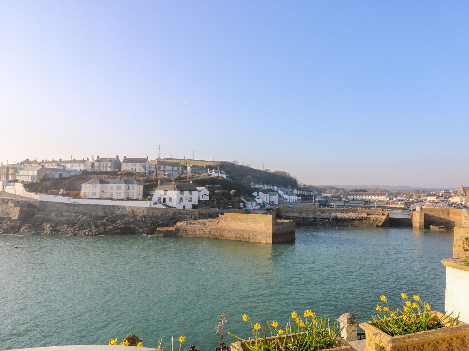 A coastal harbor with buildings along the shore and yellow flowers in the foreground at Meneage House in Helston