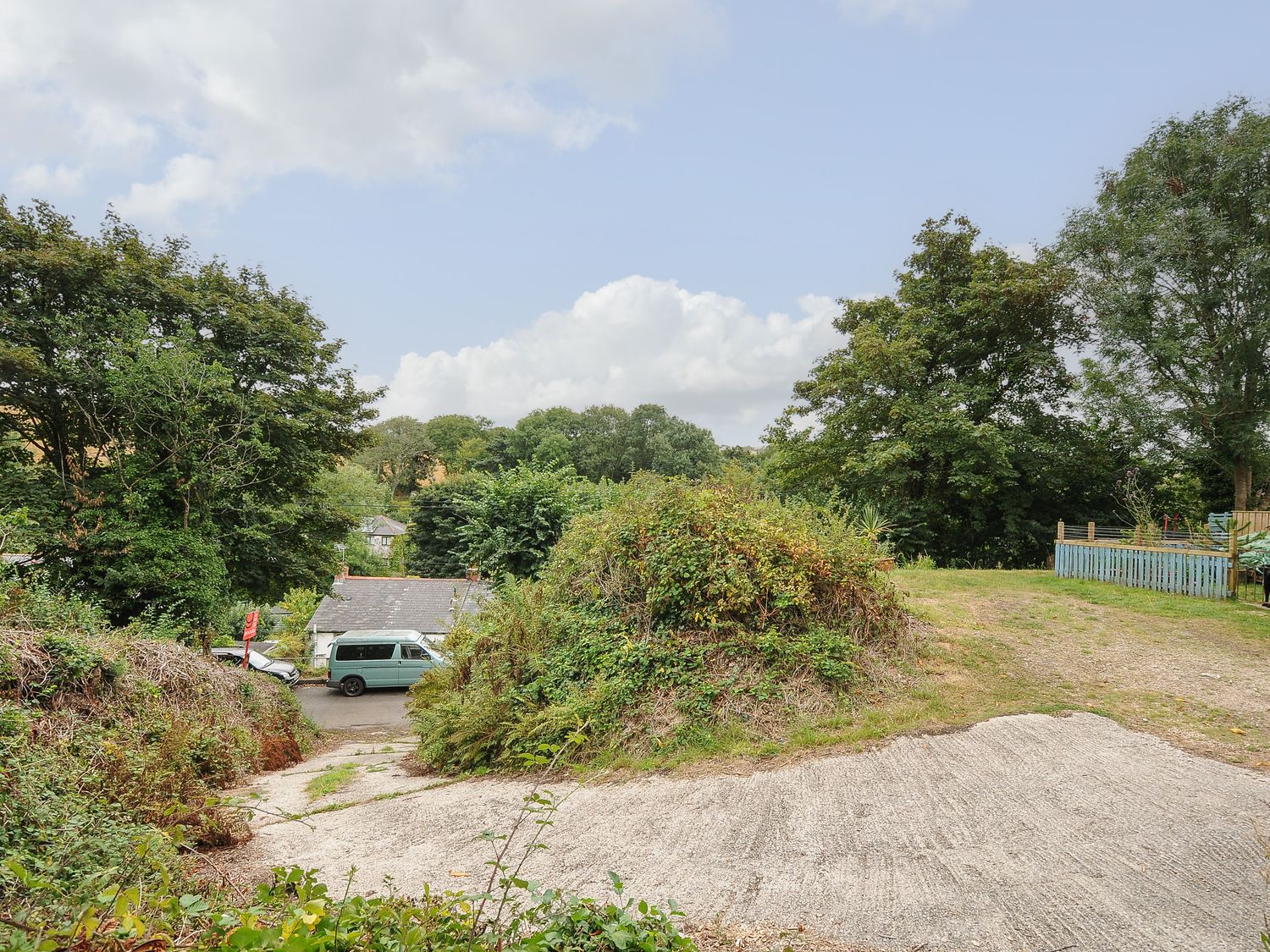 A driveway with bushes and trees leading to a road with a parked van at The Hideaway in Chacewater