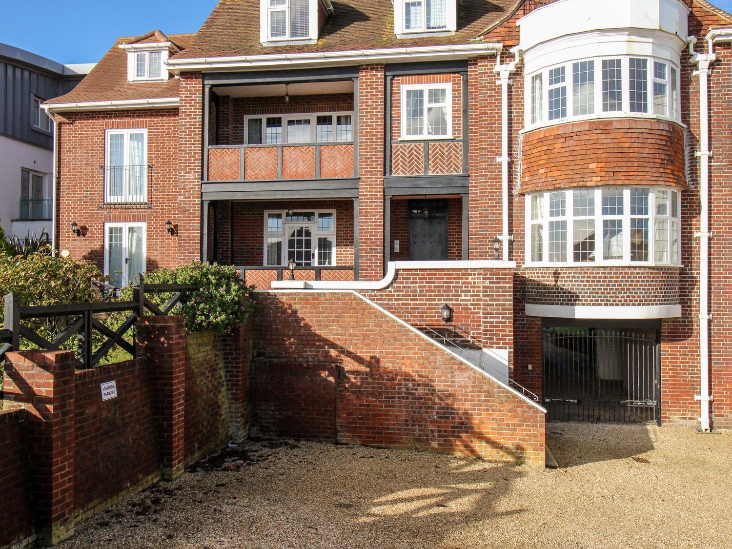 The exterior of a multi-story brick building with balconies, bay windows, steps leading to a door, and a gated driveway at Ocean Watch 5 in Greenhill