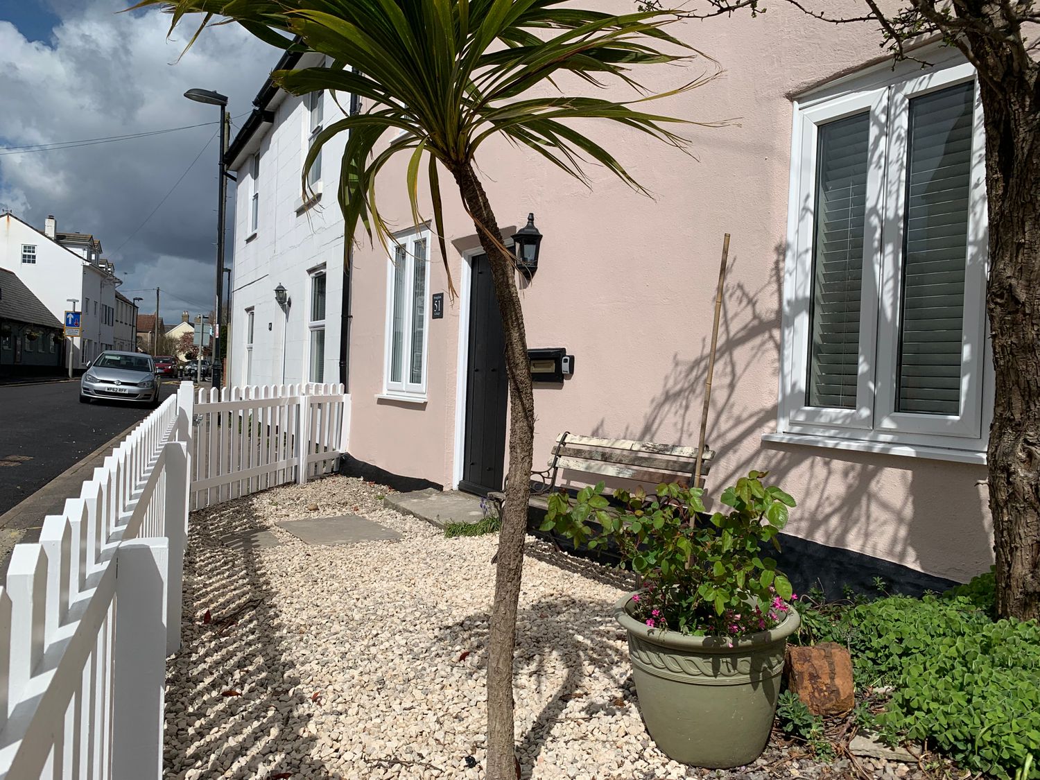 The front garden of a house with a white picket fence a potted plant a small tree and a bench outside the door at Smugglers Cottage Christchurch