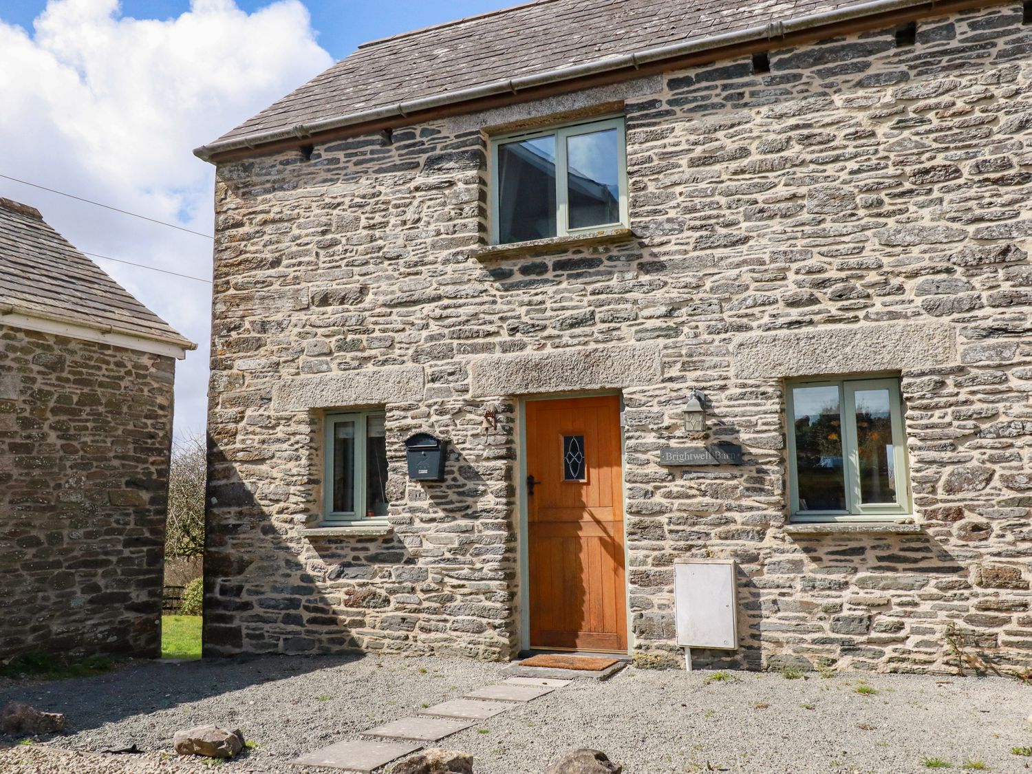 A stone house with a wooden door and three windows at Brightwell Barn Treglasta near Hallworthy