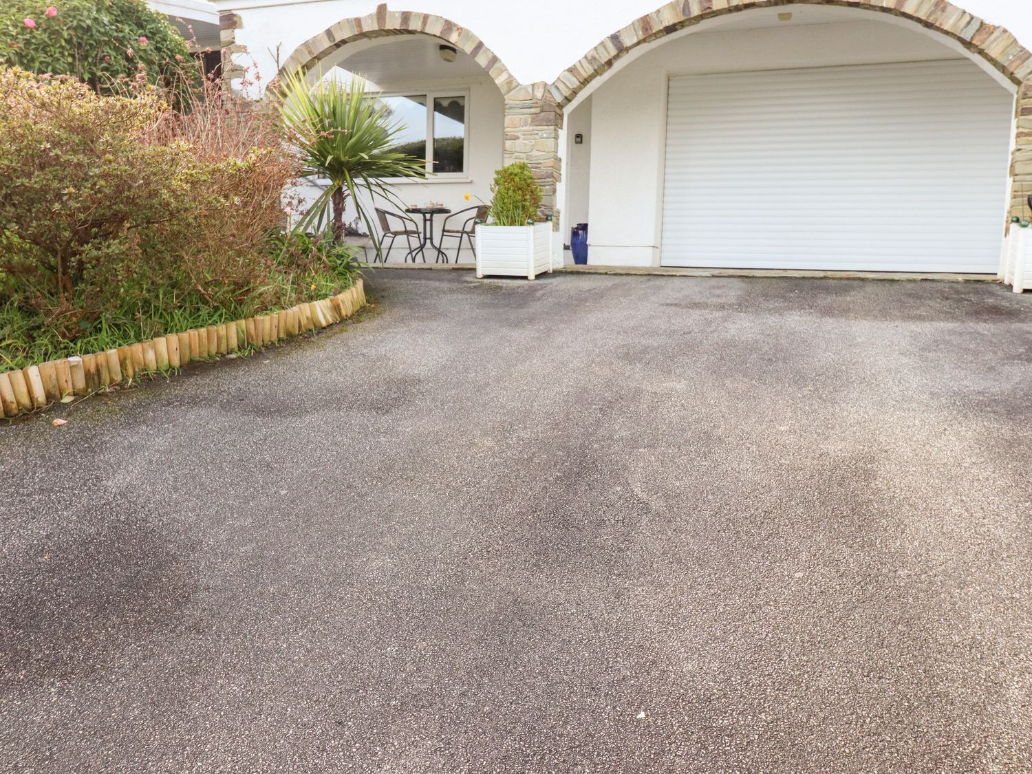 A driveway with a garage door and outdoor seating area under arches at EdyVean in Portmellon near Mevagissey