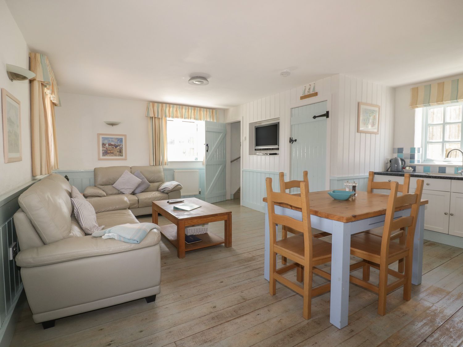 A living room with beige sofas a wooden coffee table a dining table with chairs and a kitchen area at Owls Roost in Gorran Haven
