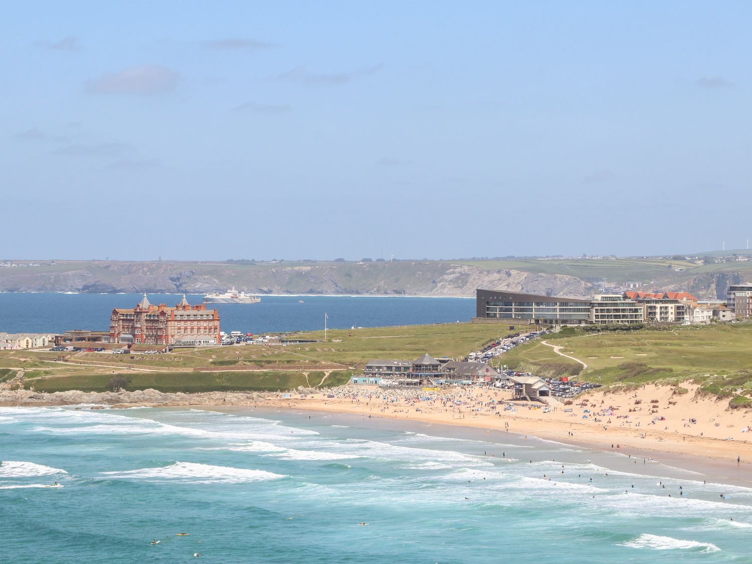 A beach with people near ocean waves with buildings and cliffs in the background at Penthouse 23 in Newquay