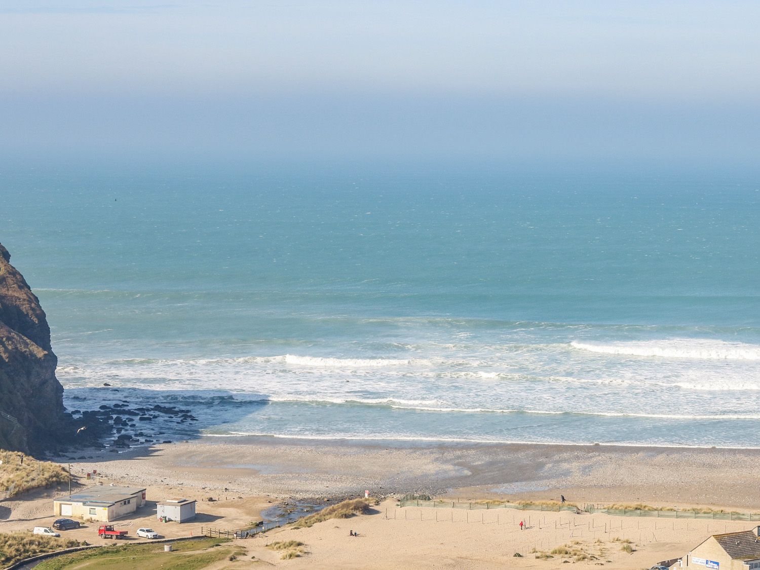 A beach with waves crashing on the shore near rocky cliffs and small buildings at 11 Towan Valley in Porthtowan