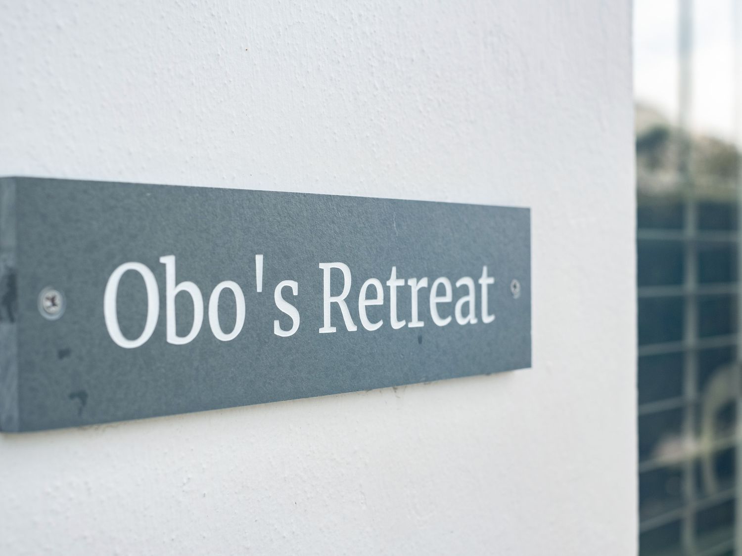 A close up of a sign reading Obos Retreat on a white wall at Obo's Retreat in St Minver near Rock