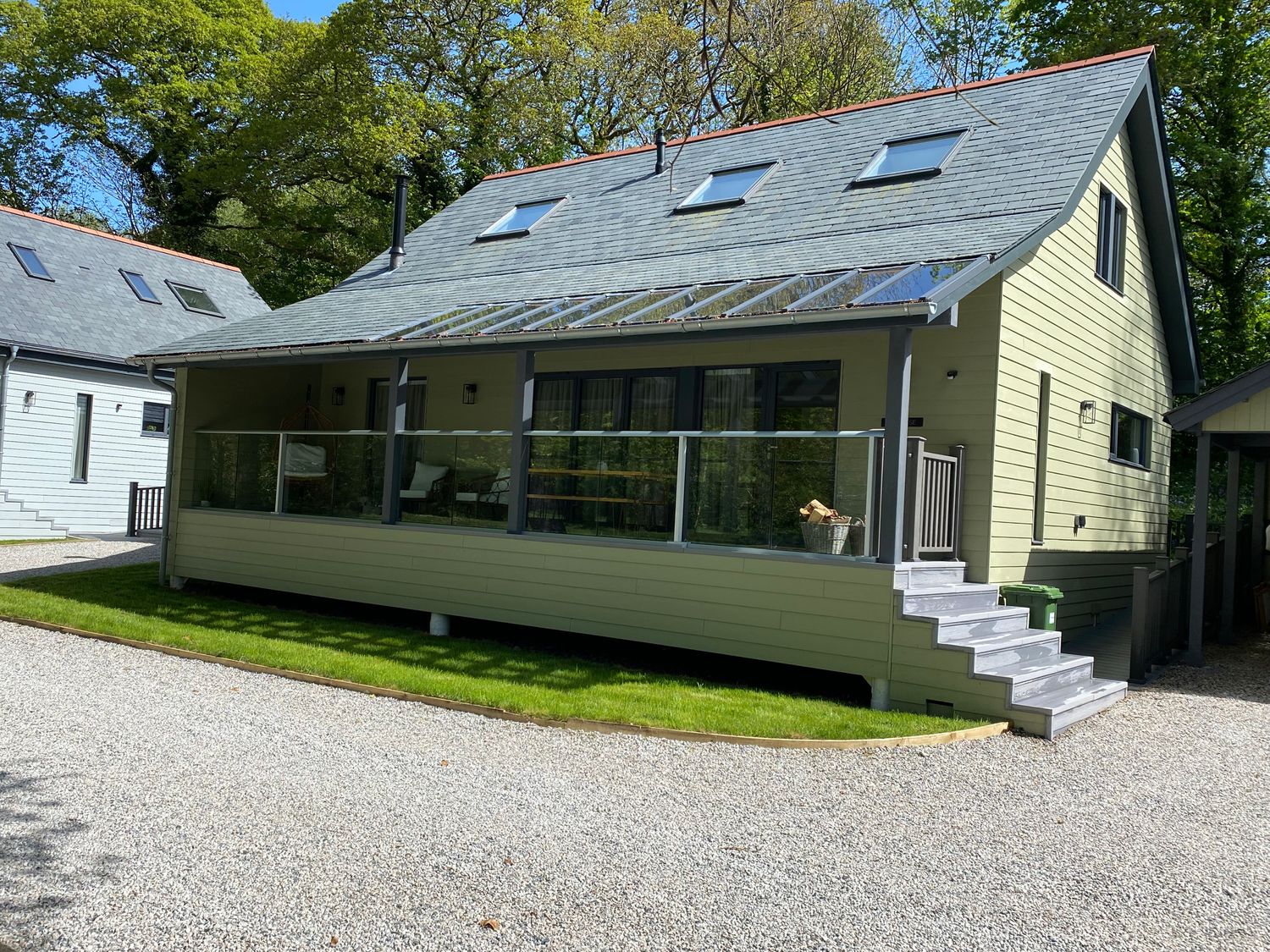 A modern house with a glass railing porch and steps on a gravel driveway surrounded by grass at Primrose Hellandbridge near Bodmin