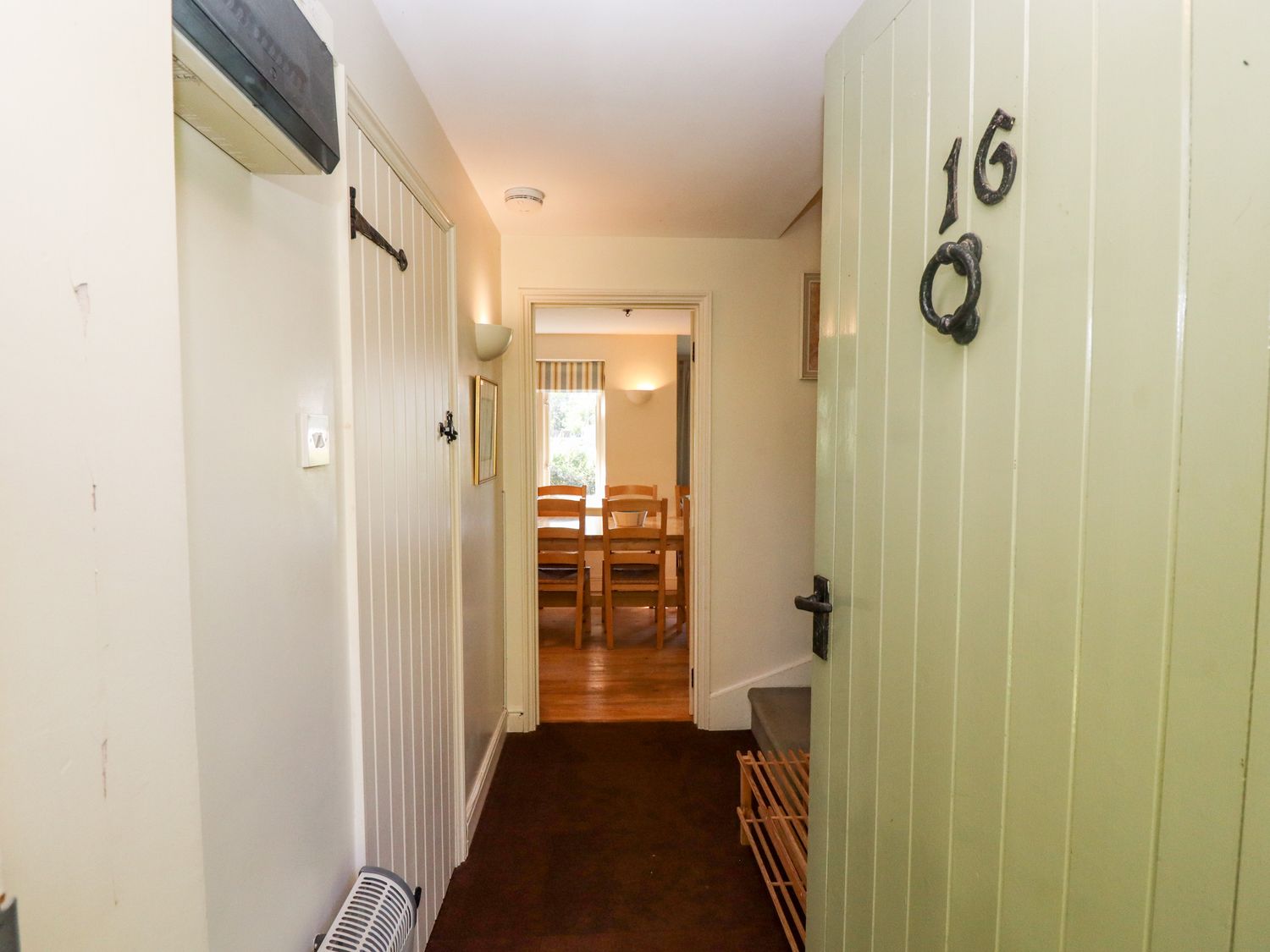 An open front door showing a hallway leading to a dining room with wooden chairs at Kingfisher House in Cotswold Water Park