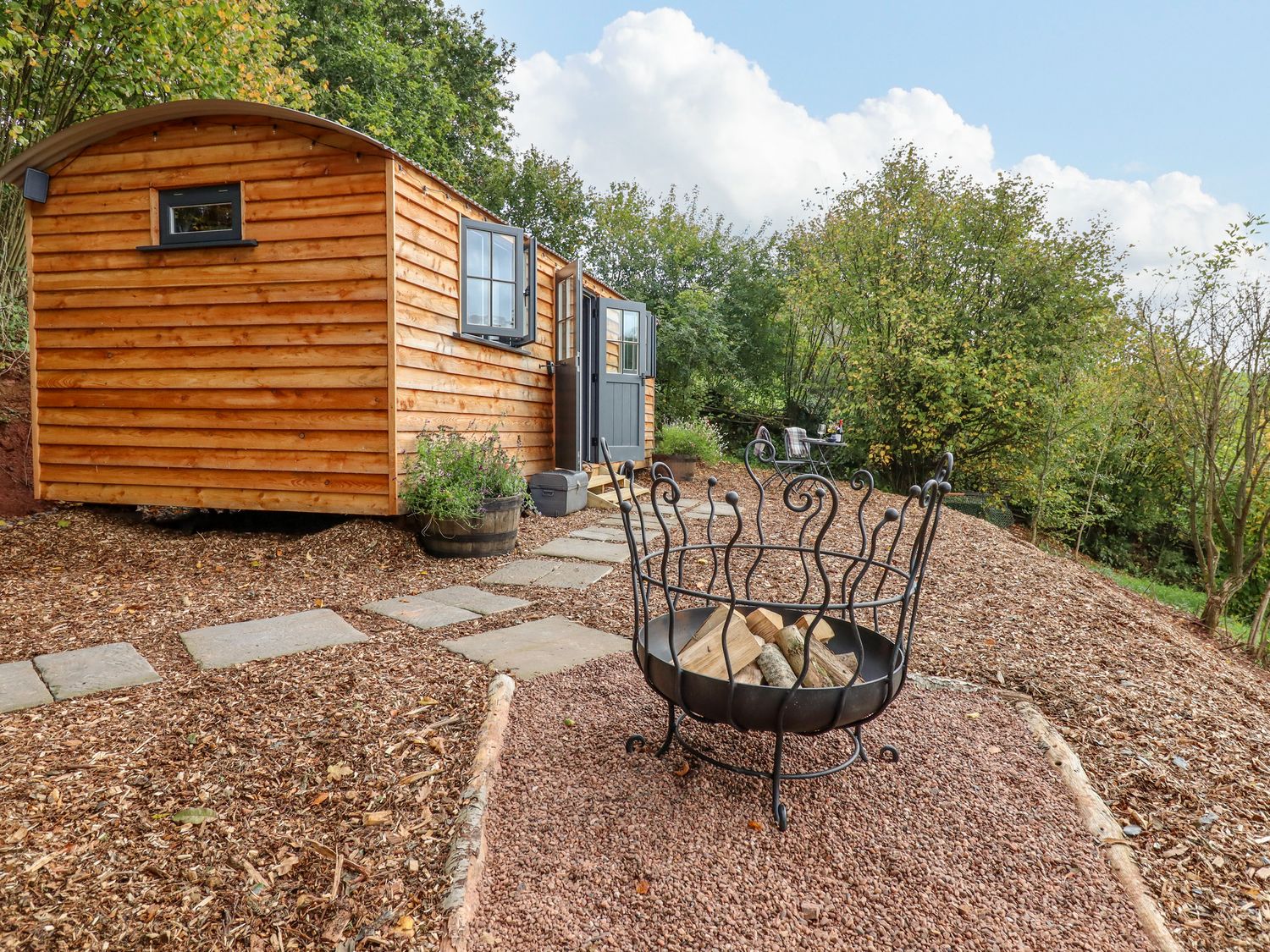 A wooden cabin with a fire pit and outdoor seating in a garden at Hideaway Cabin in Cadbury near Thorverton