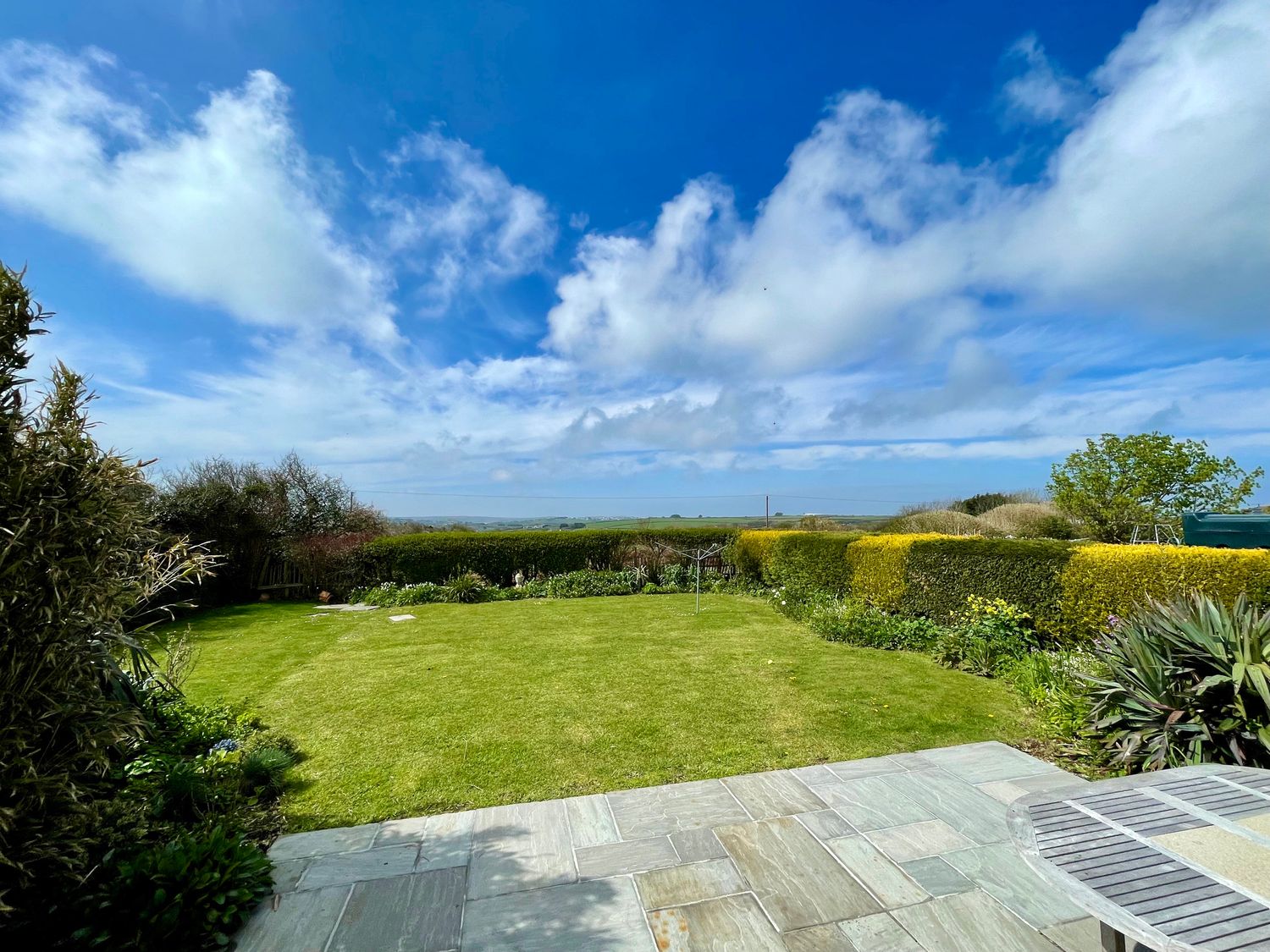 A garden with a lawn and hedges under a blue sky at Alpha in St Minver