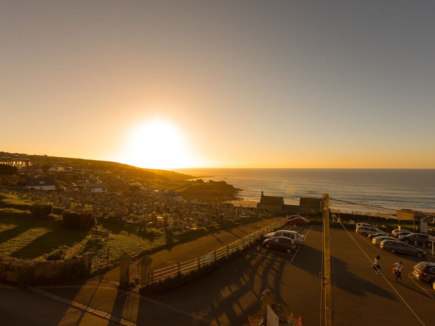 A coastal view at sunset with a parking lot and graveyard by the sea at Marchbourne in St Ives
