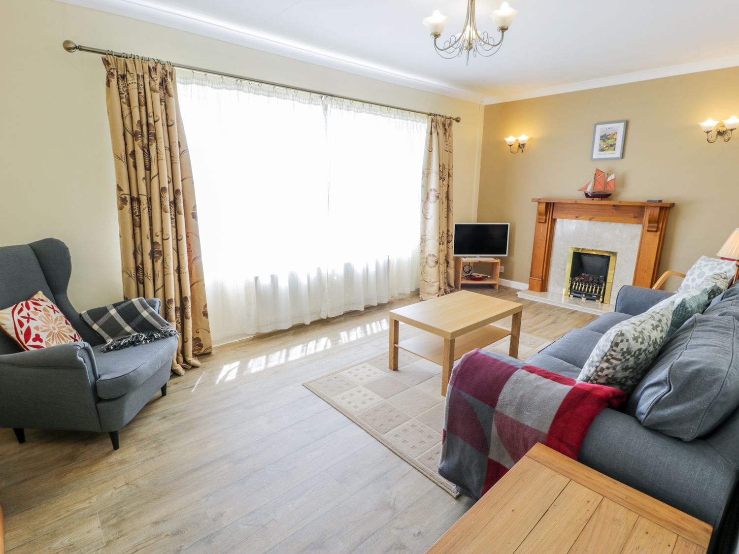 A living room with a gray armchair a sofa a wooden coffee table a fireplace and a television at Ceris in Penrhyndeudraeth