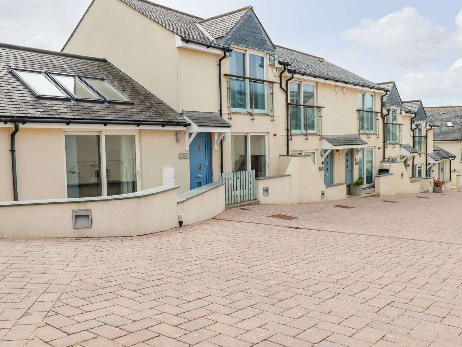 A row of modern townhouses with blue doors and glass balconies on a paved street at Constantine Bay Cottage in Constantine Bay