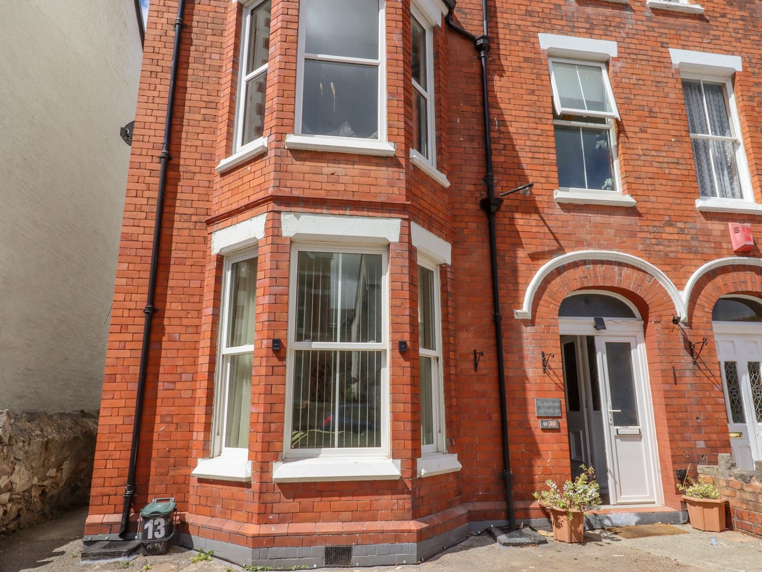 The exterior of a red brick building with white window frames and a door at The Bookcase in Colwyn Bay