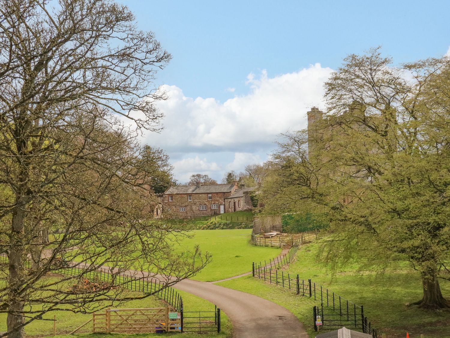 A country road leading to stone buildings surrounded by green fields and trees at South Lodge in Appleby-In-Westmorland