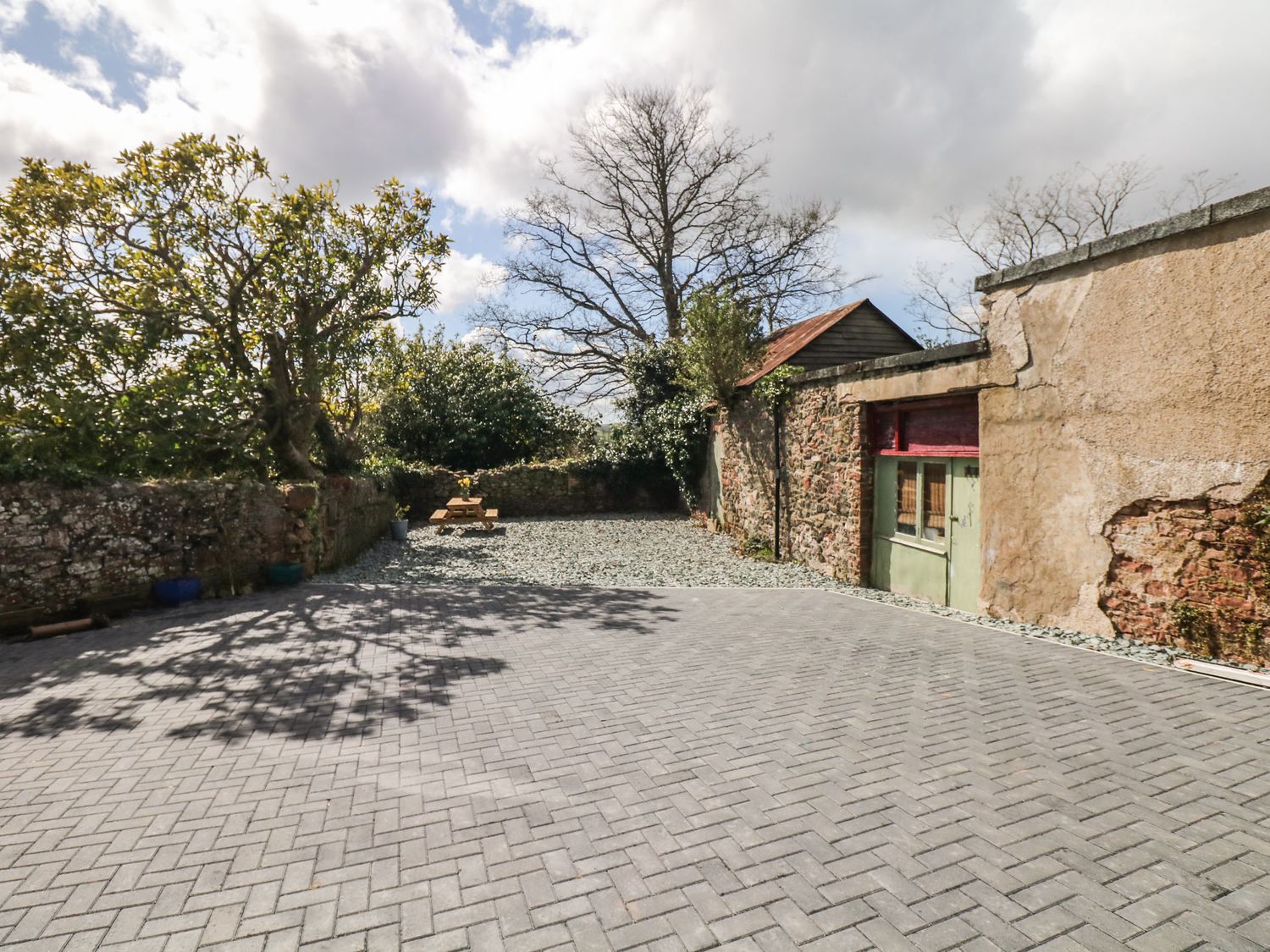An outdoor courtyard with brick paving a picnic table a stone wall and trees at Valley View in Bishopsteignton