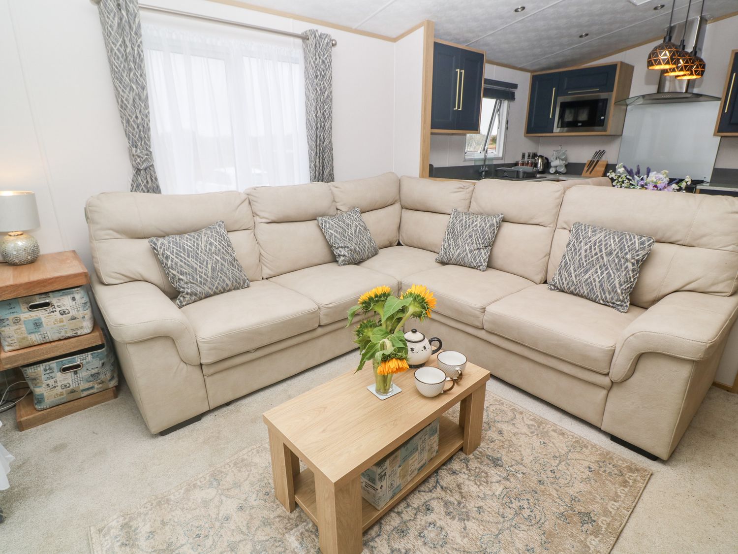 A living room with a beige sectional sofa and patterned cushions at Chantry Lodge in Hendra Croft near Goonhavern