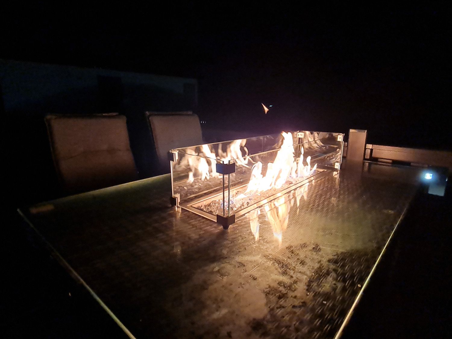 An outdoor table with a rectangular fire pit and chairs in the dark at Chantry Lodge in Hendra Croft near Goonhavern