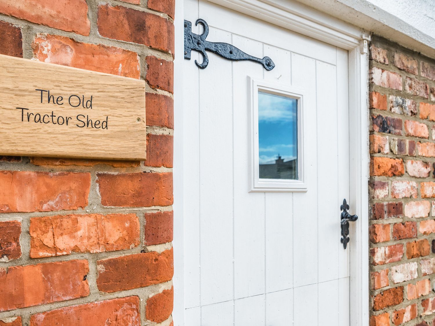 A white door with a small window and black metal hardware next to a brick wall with a sign saying The Old Tractor Shed at The Old Tractor Shed in Skipsea
