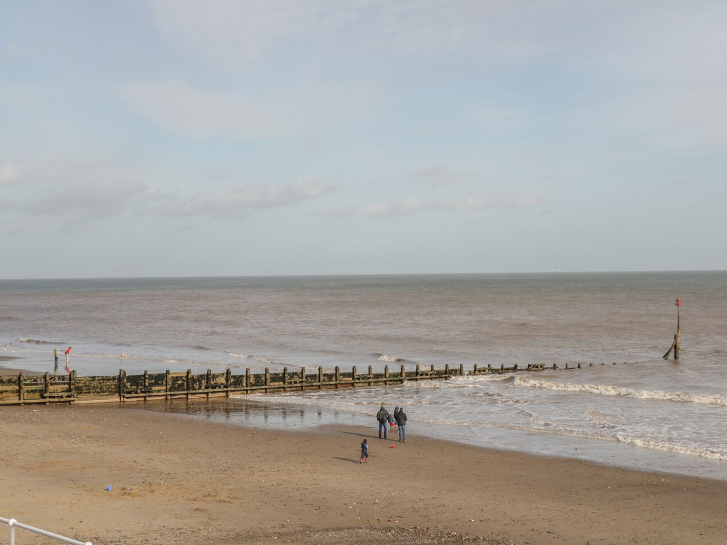 A beach with people walking near wooden groynes and the sea at The Old Tractor Shed in Skipsea