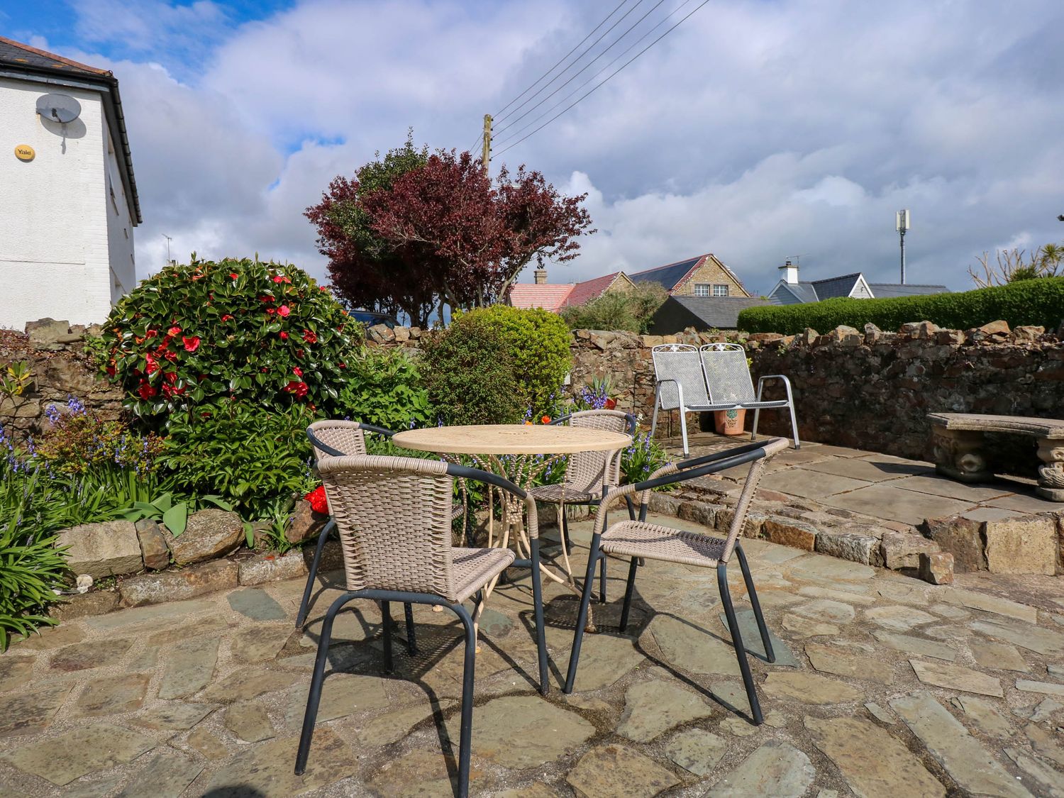 An outdoor patio with a round table and four chairs surrounded by plants and a stone wall at Angorfa Bach in Abersoch
