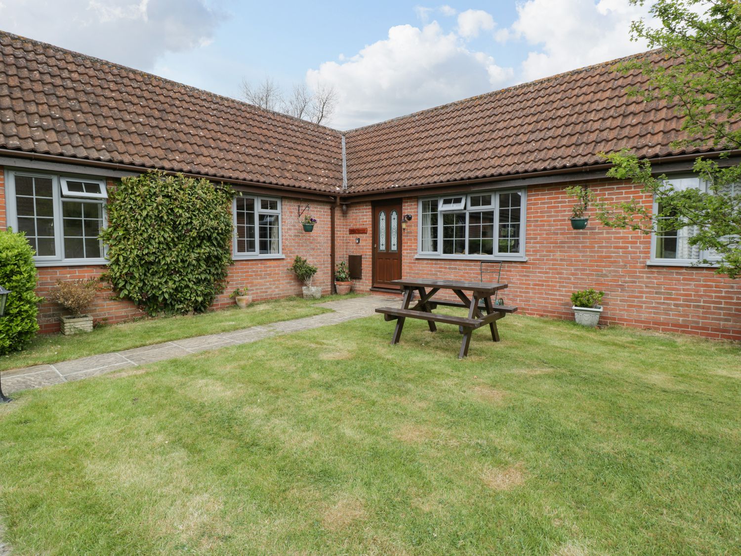 An outdoor courtyard with a wooden picnic table green grass brick walls and windows at Owls Retreat in Brean