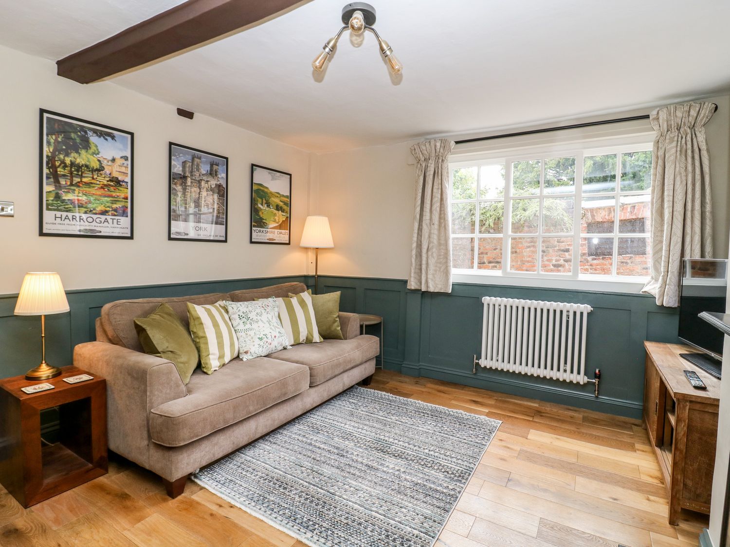 A living room with a brown sofa and cushions a rug on wooden floor and framed pictures on the wall at Kemps Yard Retreat in Thirsk