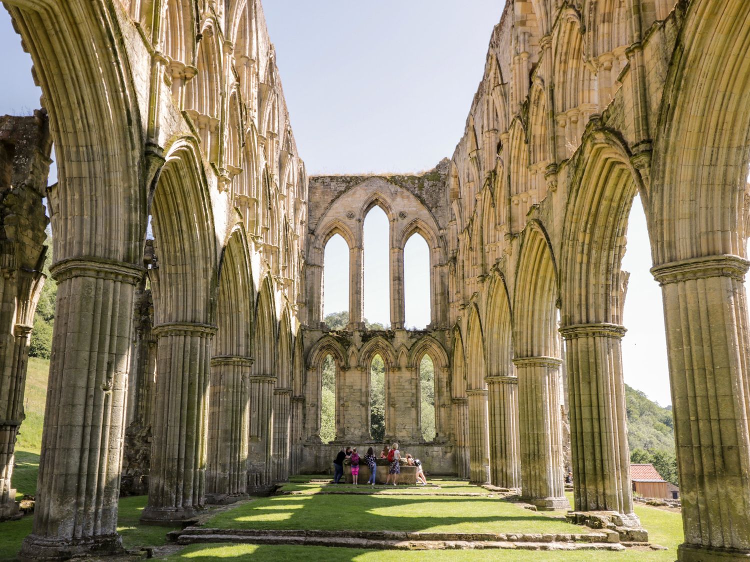 Ruins of a large stone building with tall arches and columns with people gathered inside on grass at Kemps Yard Retreat in Thirsk