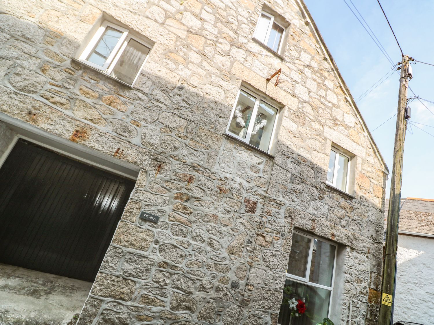 A stone house with multiple windows and a wooden door with a sign that says Troika in Newlyn