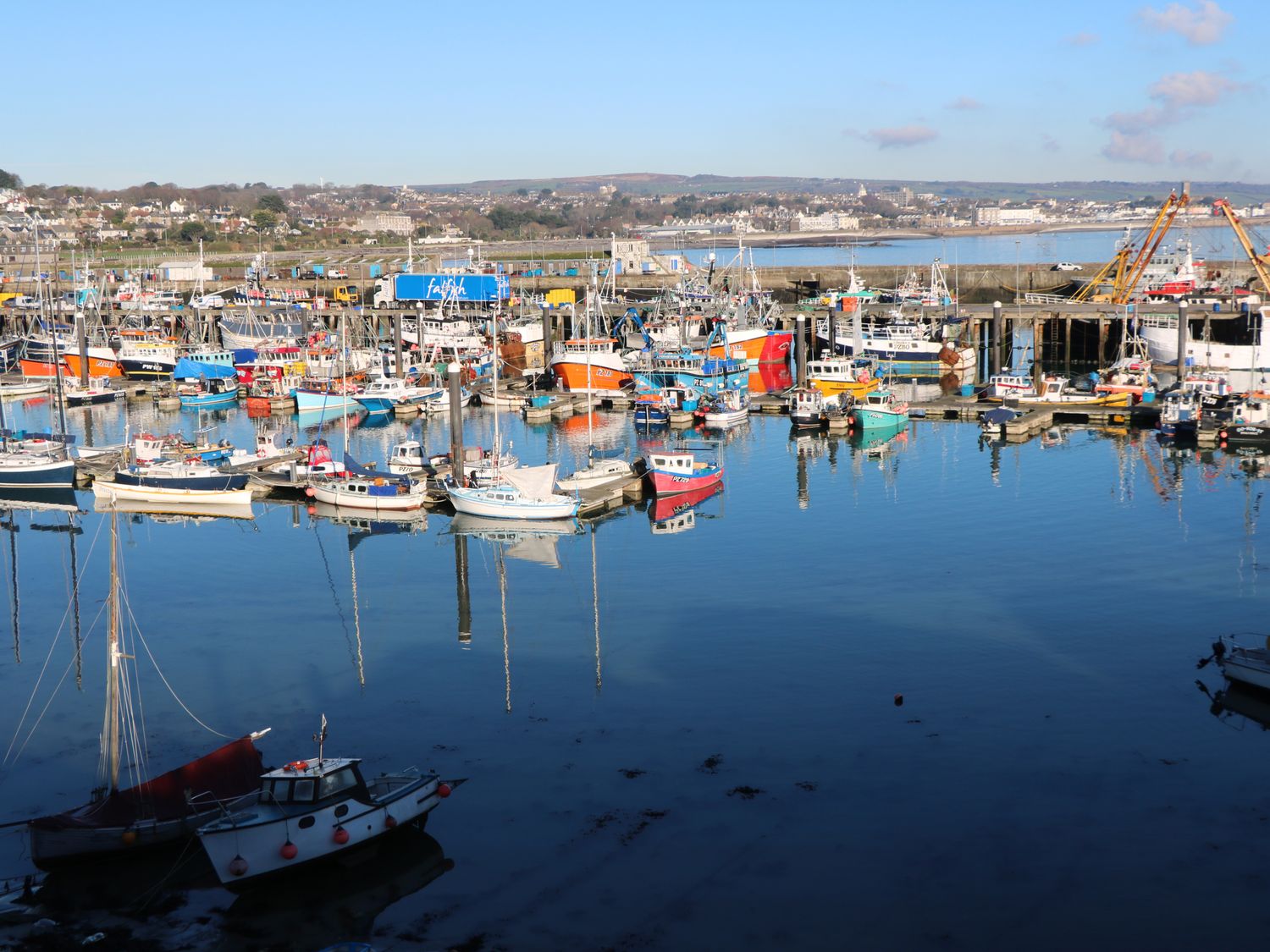 A harbor with many fishing boats on water and a town in the background at Troika in Newlyn